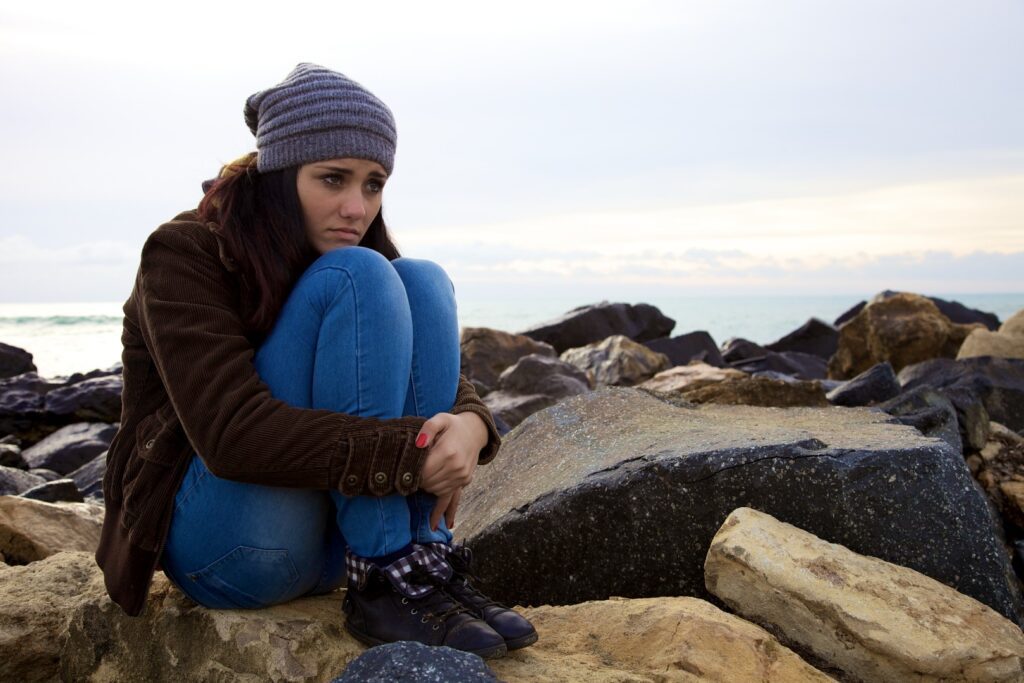 A woman sitting on top of rocks near the ocean.