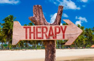 A wooden sign that says therapy with an arrow pointing to the right.