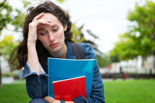 A woman sitting on the grass holding two books.