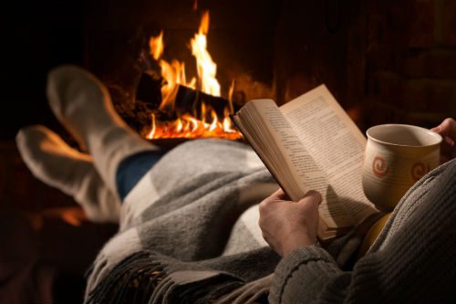 A person laying in front of a fire reading